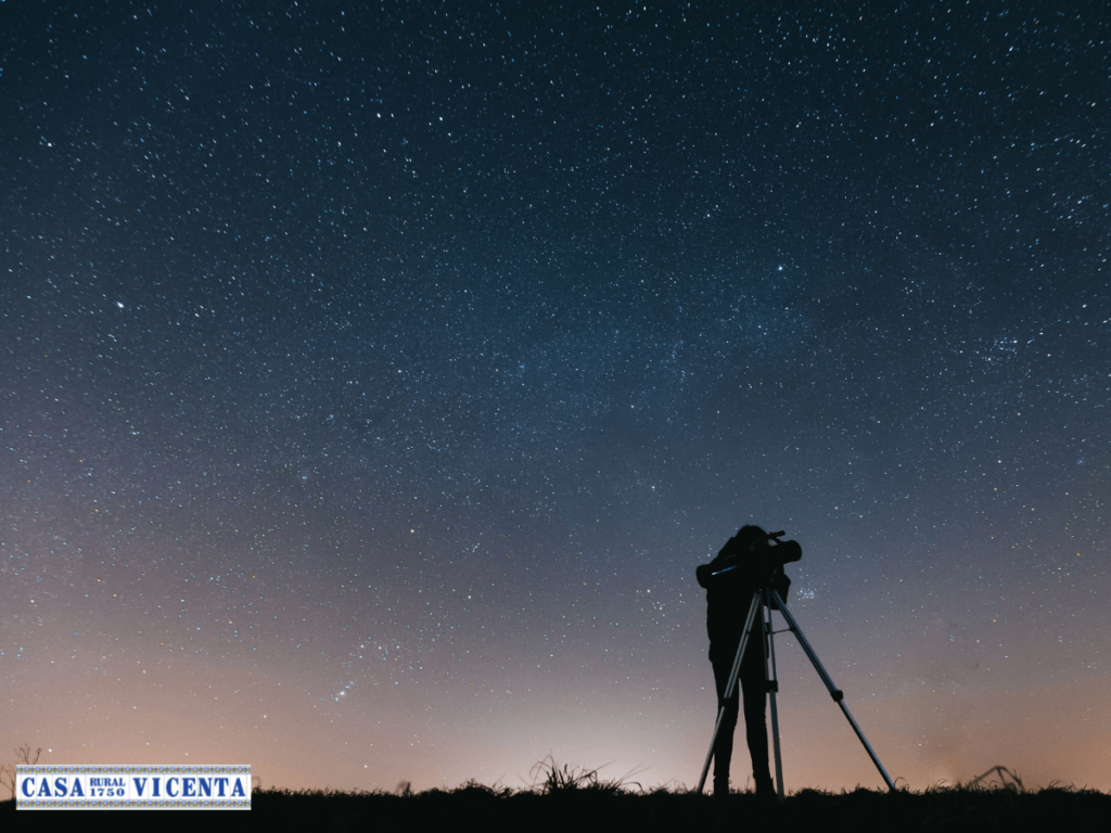 Señor con una cámara y un trípode con las estrellas de fondo